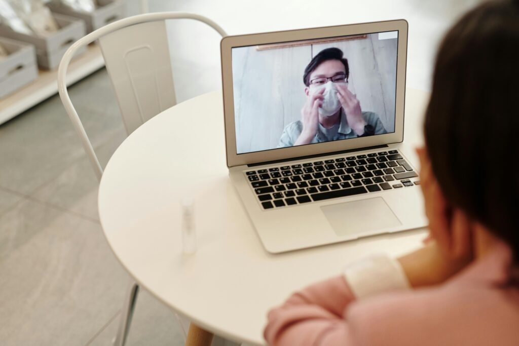 Person in a virtual medical consultation with a doctor on a laptop wearing a face mask.